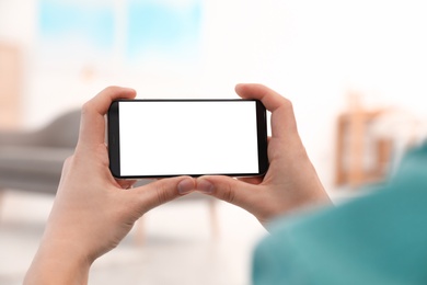 Photo of Man holding smartphone with blank screen indoors, closeup of hands. Space for text