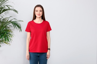 Photo of Young woman in t-shirt near light wall. Mock up for design