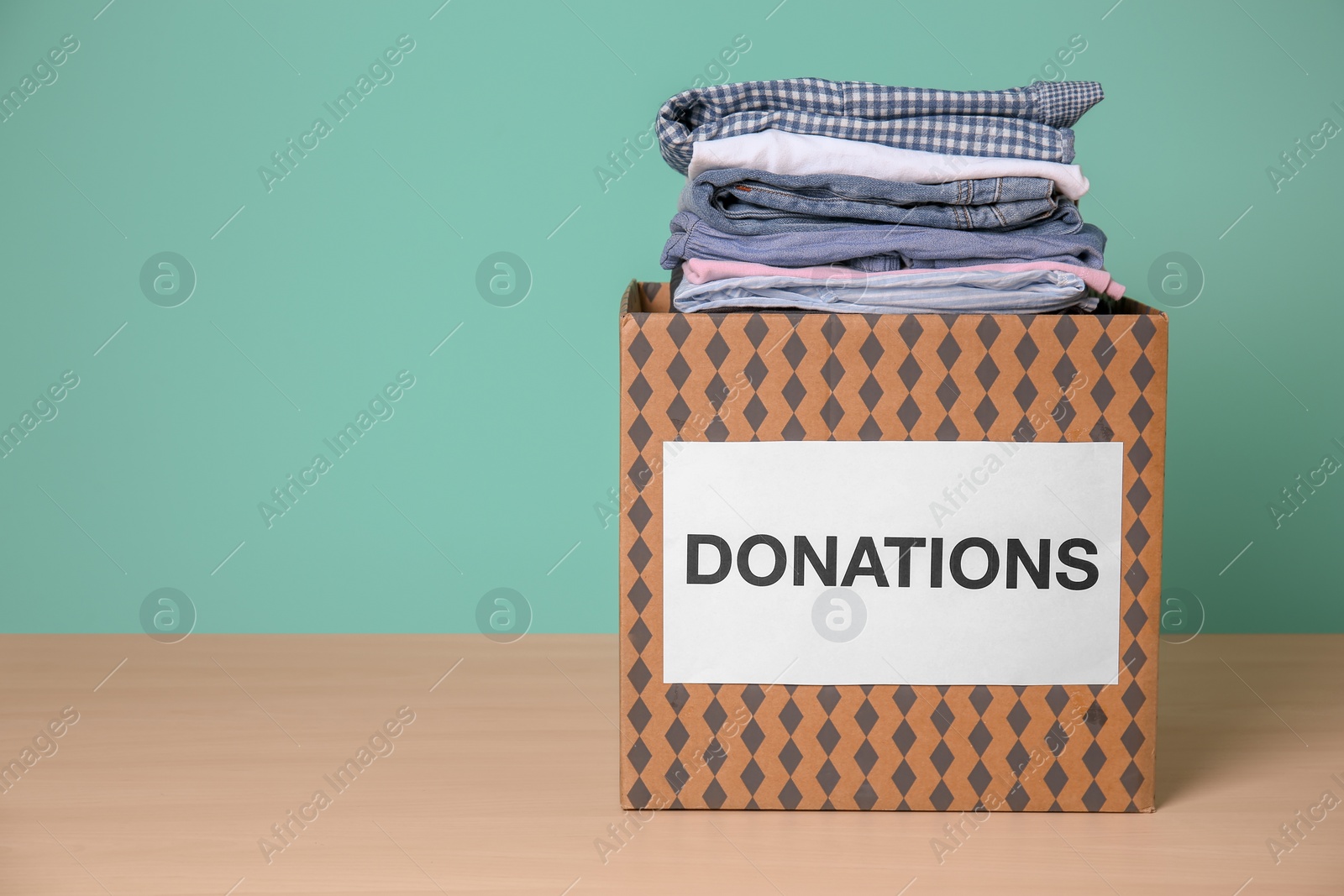 Photo of Donation box with clothes on wooden table against color background