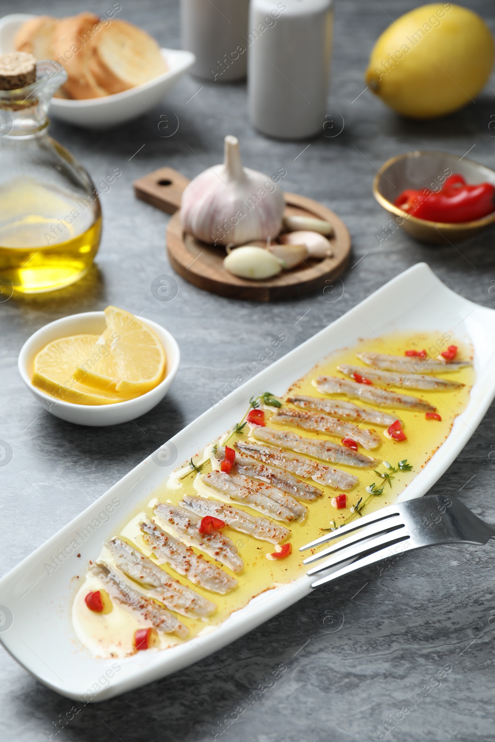 Photo of Tasty pickled anchovies with spices and products on gray table