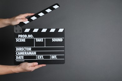 Photo of Woman holding clapperboard on dark grey background, closeup with space for text. Cinema production