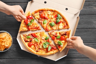 People taking slices of delicious pizza with tomatoes and sausages at table