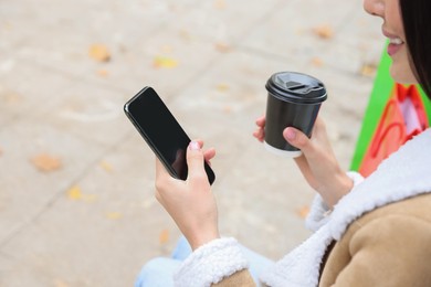 Special Promotion. Young woman with smartphone and cup of drink outdoors, closeup