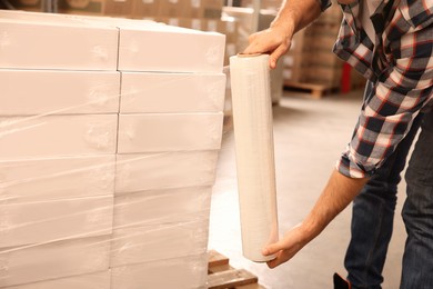 Worker wrapping boxes in stretch film at warehouse, closeup