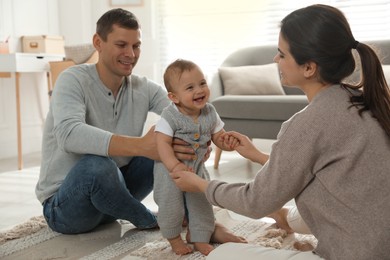 Photo of Parents supporting their baby daughter while she learning to walk at home