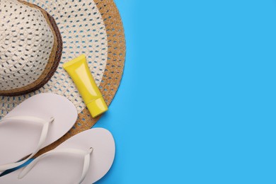 Photo of Straw hat, sunscreen and flip flops on light blue background, flat lay and space for text. Beach accessories