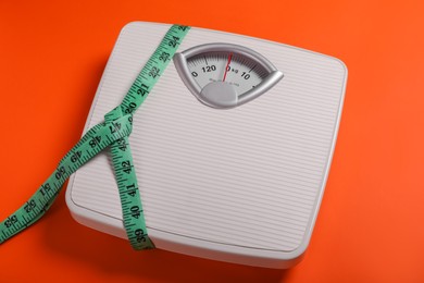 Photo of Scales and measuring tape on orange background. Weight loss concept