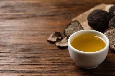 Photo of Fresh truffle oil in bowl on wooden table, space for text