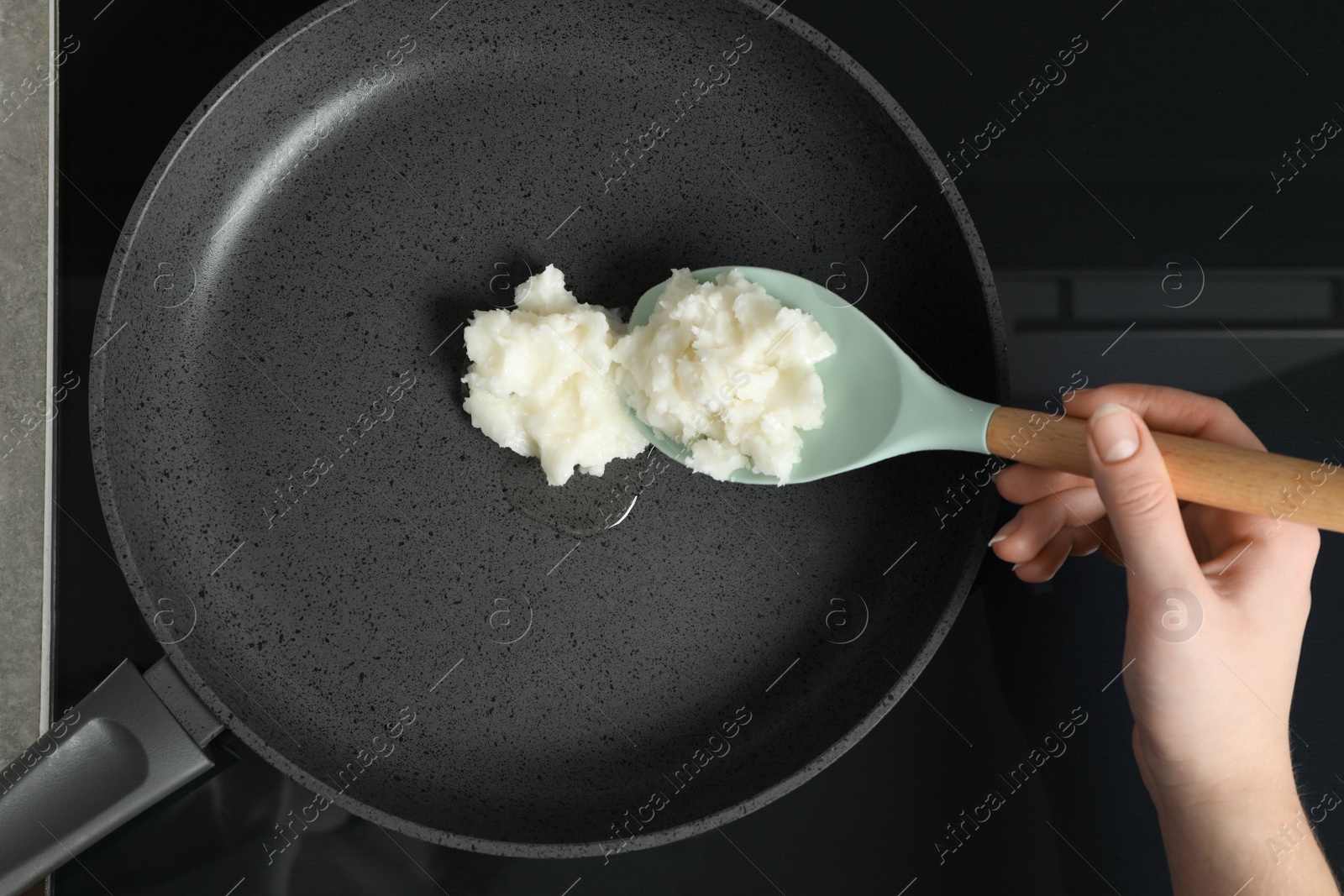 Photo of Woman cooking with coconut oil on induction stove, top view