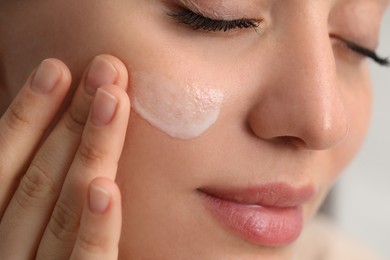 Photo of Young woman with dry skin applying cream onto her face, closeup