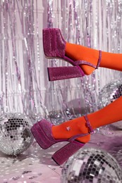 Photo of Woman in orange tights and pink high heeled shoes among disco balls indoors, closeup