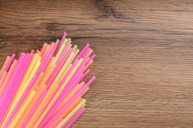 Colorful plastic drinking straws on wooden table, flat lay. Space for text