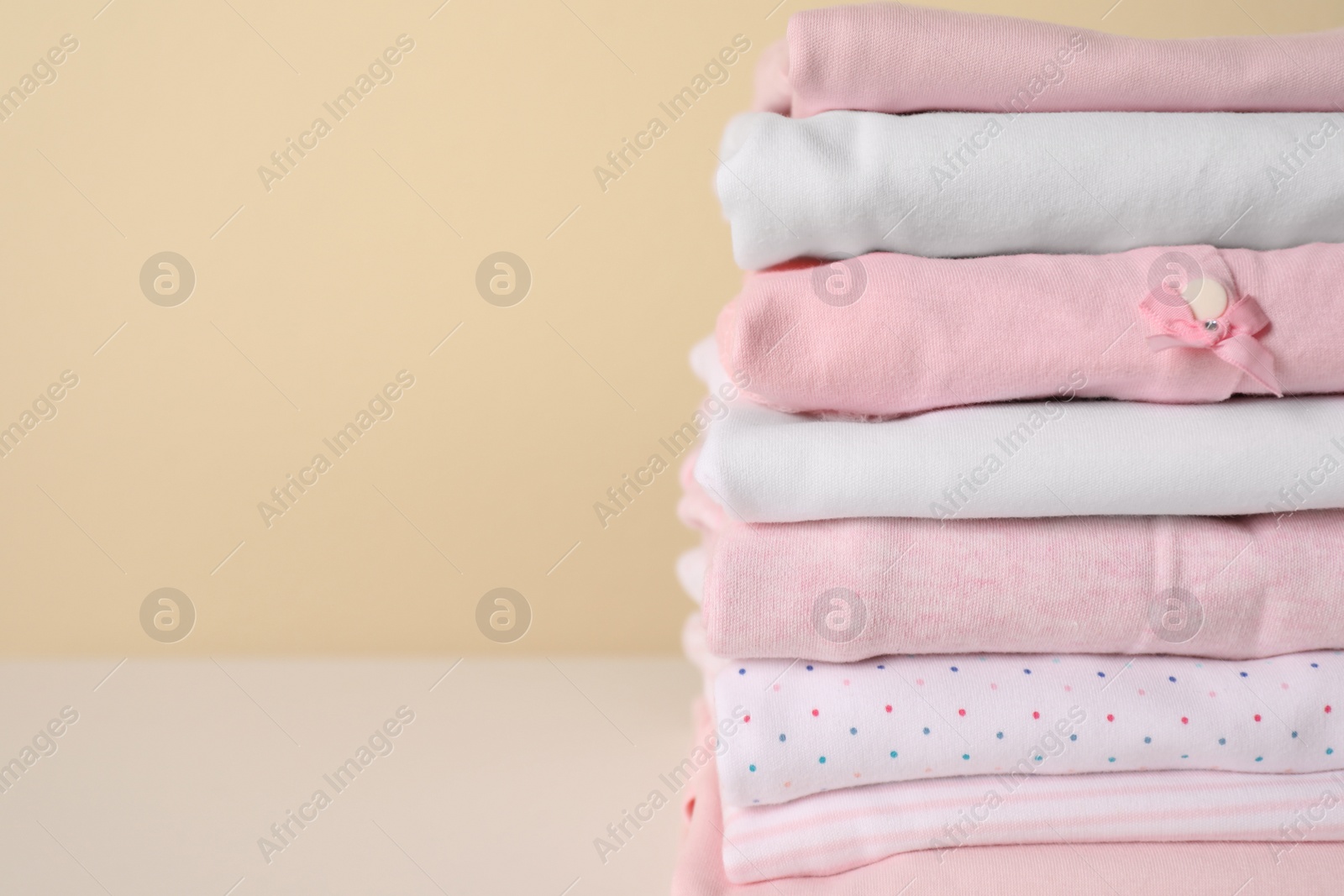 Photo of Stack of baby girl's clothes on white table, closeup. Space for text