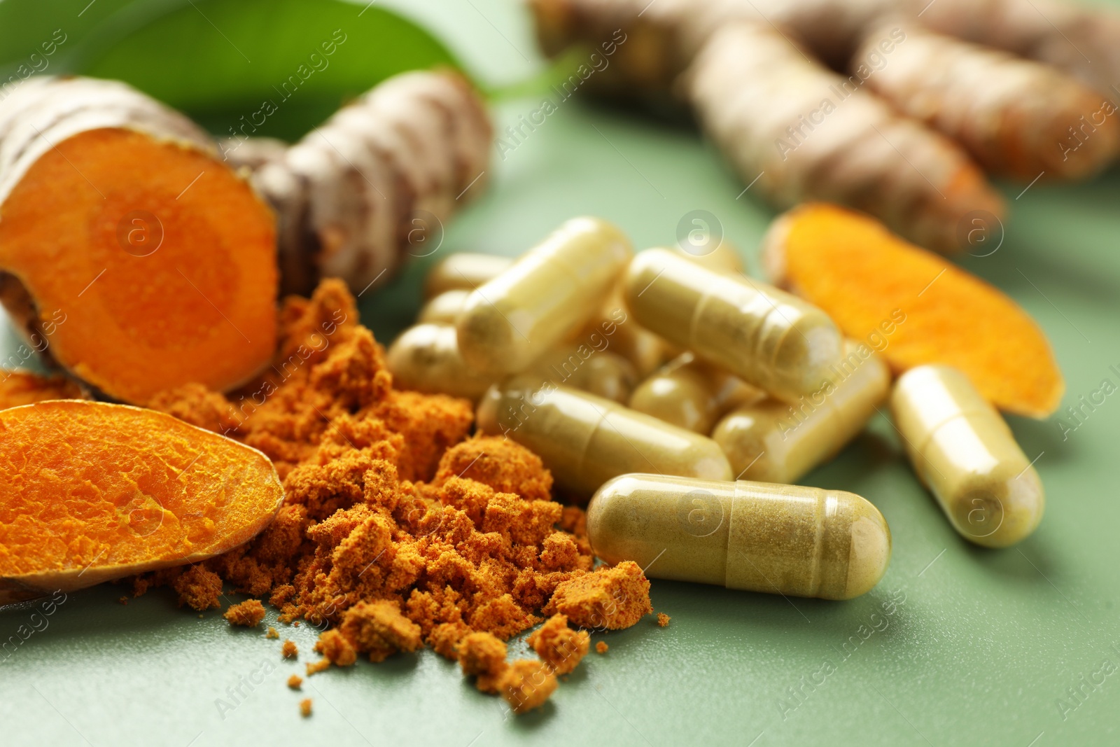 Photo of Aromatic turmeric powder, pills and raw roots on green background, closeup