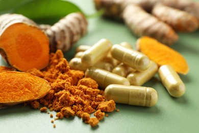 Aromatic turmeric powder, pills and raw roots on green background, closeup