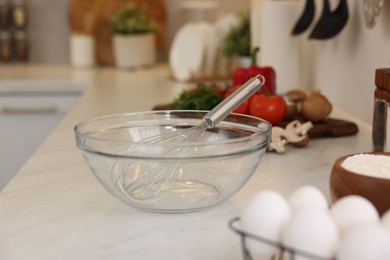 Metal whisk, bowl and different products on light table in kitchen