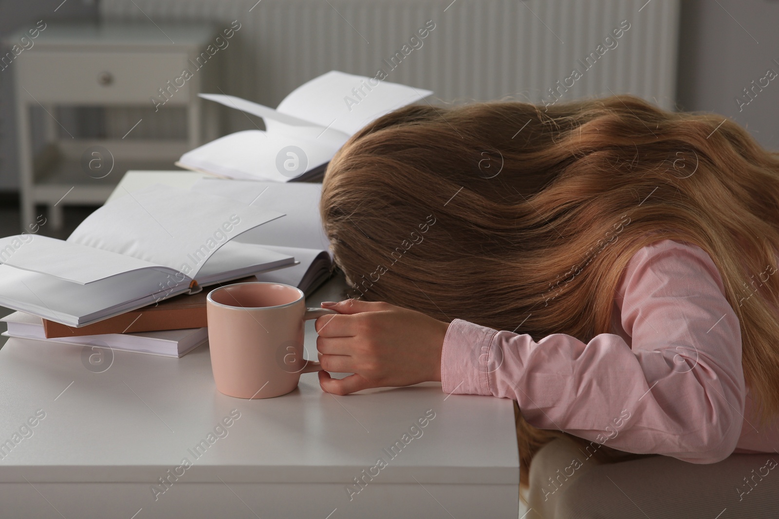 Photo of Young tired woman sleeping near books at white table indoors