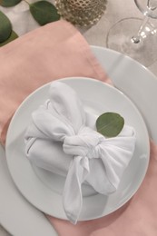 Photo of Furoshiki technique. Gift packed in white fabric and eucalyptus leaves on table, flat lay