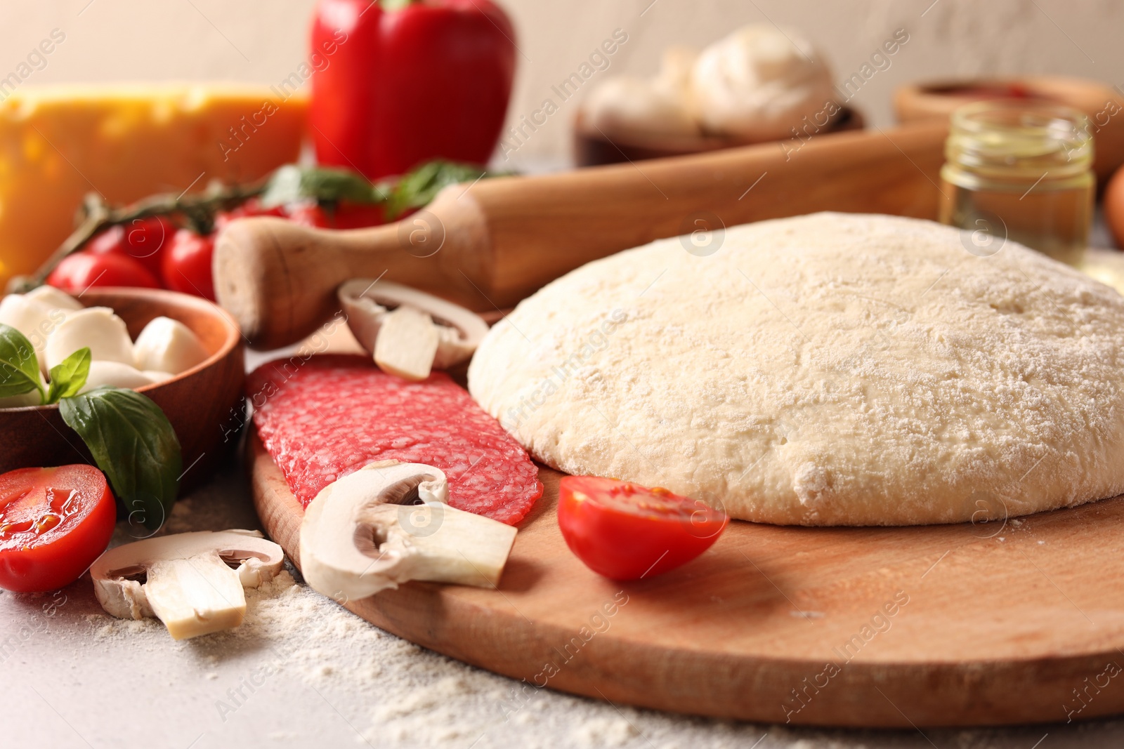 Photo of Pizza dough, products and rolling pin on gray table, closeup