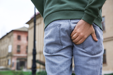 Photo of Man suffering from hemorrhoid pain outdoors, back view