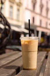 Photo of Takeaway plastic cup with cold coffee drink and straw on wooden bench outdoors
