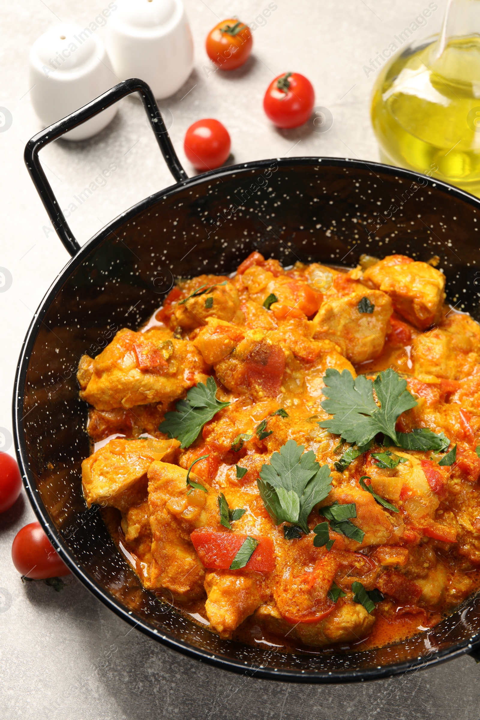 Photo of Delicious chicken curry in frying pan and tomatoes on light grey table