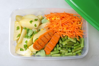 Tasty potatoes with cutlets and vegetables in plastic container on light table, top view