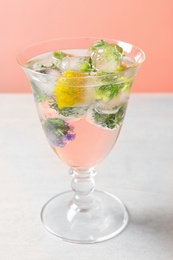 Glass of ice cubes with flowers on light table against pink background