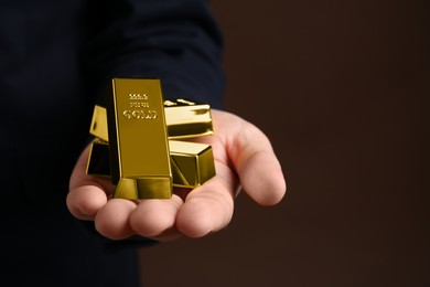 Man holding gold bars on brown background, closeup. Space for text