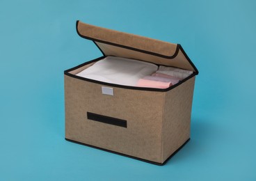 Photo of Textile storage case with folded clothes on light blue background