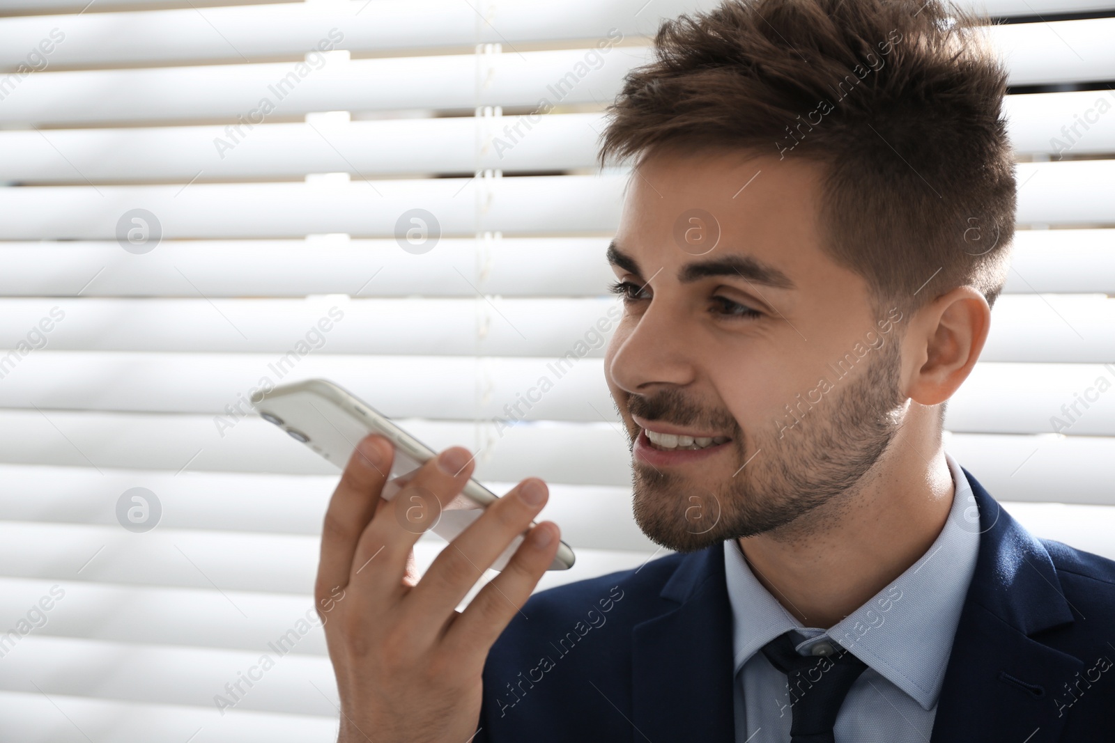 Photo of Young man using voice search on smartphone indoors