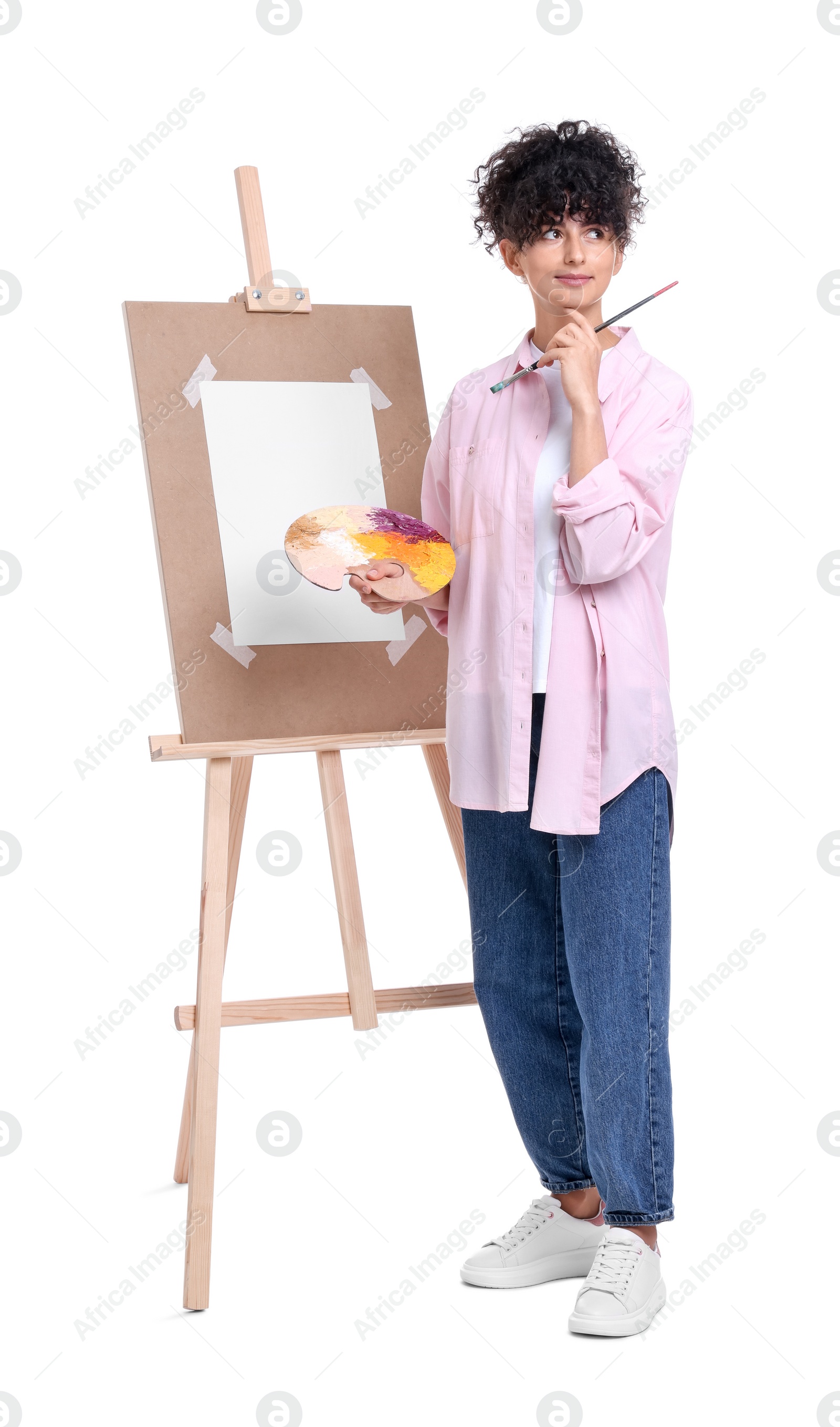 Photo of Young woman holding brush and artist`s palette near easel against white background