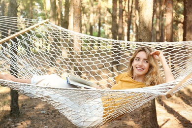 Photo of Happy young woman with book relaxing in hammock outdoors on summer day