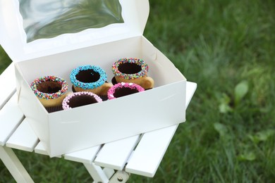Box of delicious edible biscuit coffee cups decorated with sprinkles on white wooden table outdoors, space for text