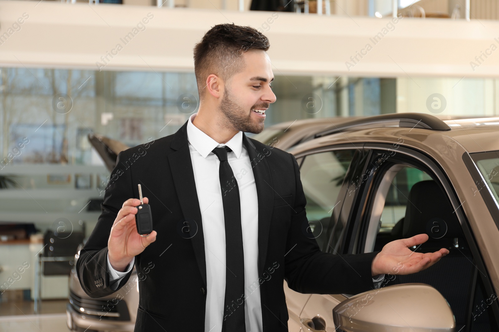 Photo of Young salesman with key near car in dealership