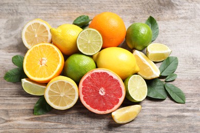 Different fresh citrus fruits and leaves on wooden table, closeup