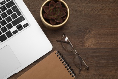 Modern laptop, notebook, glasses and houseplant on wooden table, flat lay. Space for text