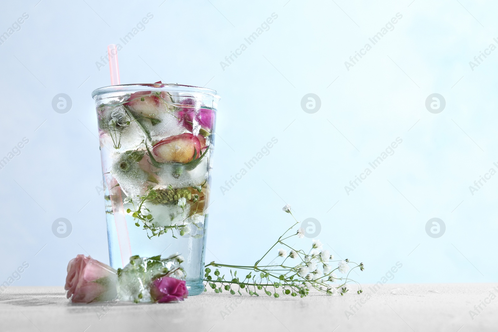 Photo of Glass of water with ice cubes and flowers on table against color background, space for text