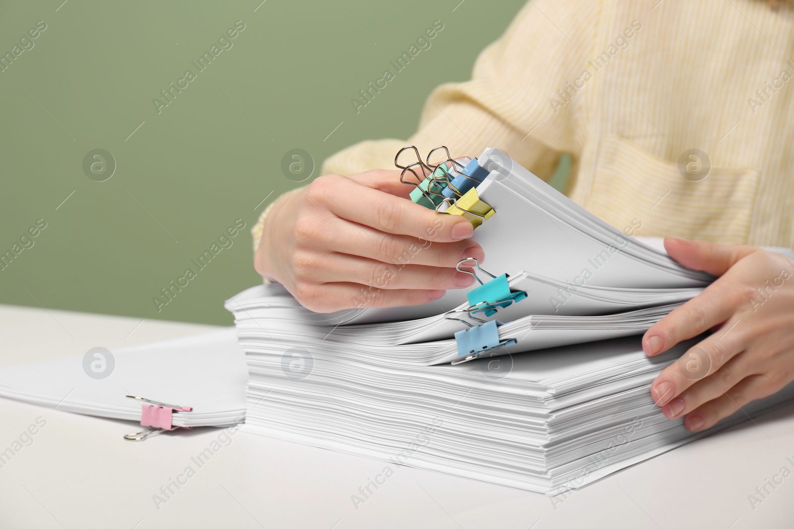 Photo of Woman stacking documents at white table against green background, closeup