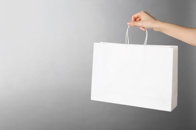 Woman holding white paper bag on grey background, closeup with space for text. Mockup for design