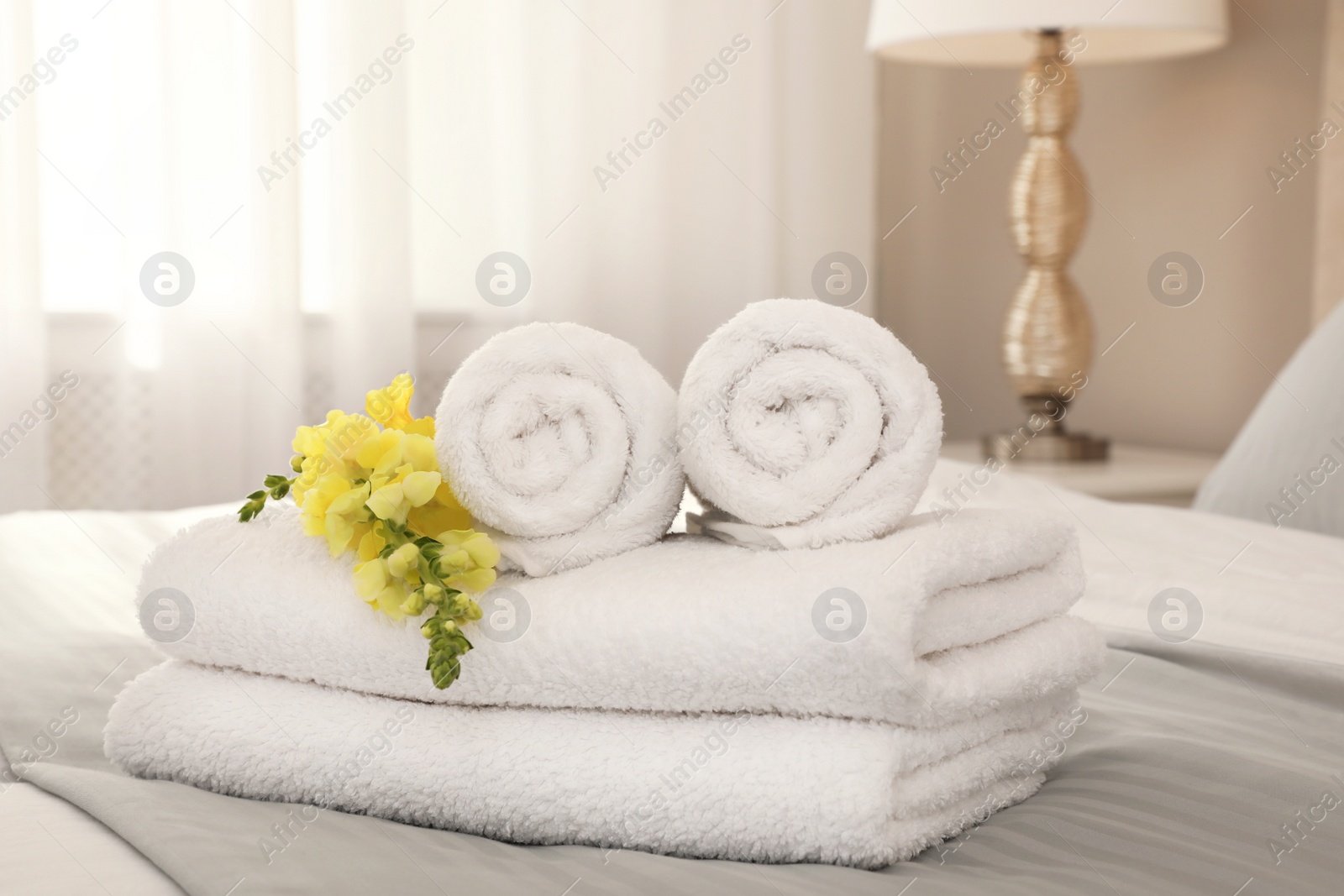 Photo of Fresh white towels with flower on bed indoors