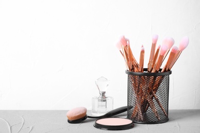 Photo of Make up brushes in holder and cosmetic products on grey table. Space for text