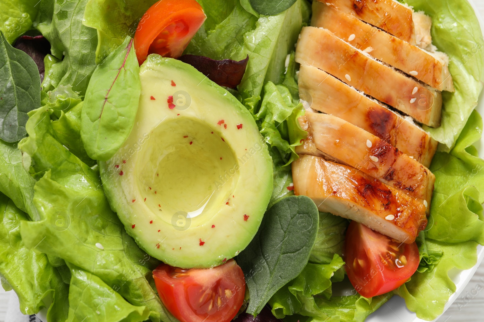 Photo of Delicious salad with chicken, cherry tomato and avocado in bowl, top view