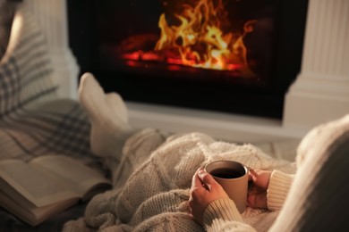 Woman with cup near fireplace indoors, closeup. Cozy atmosphere