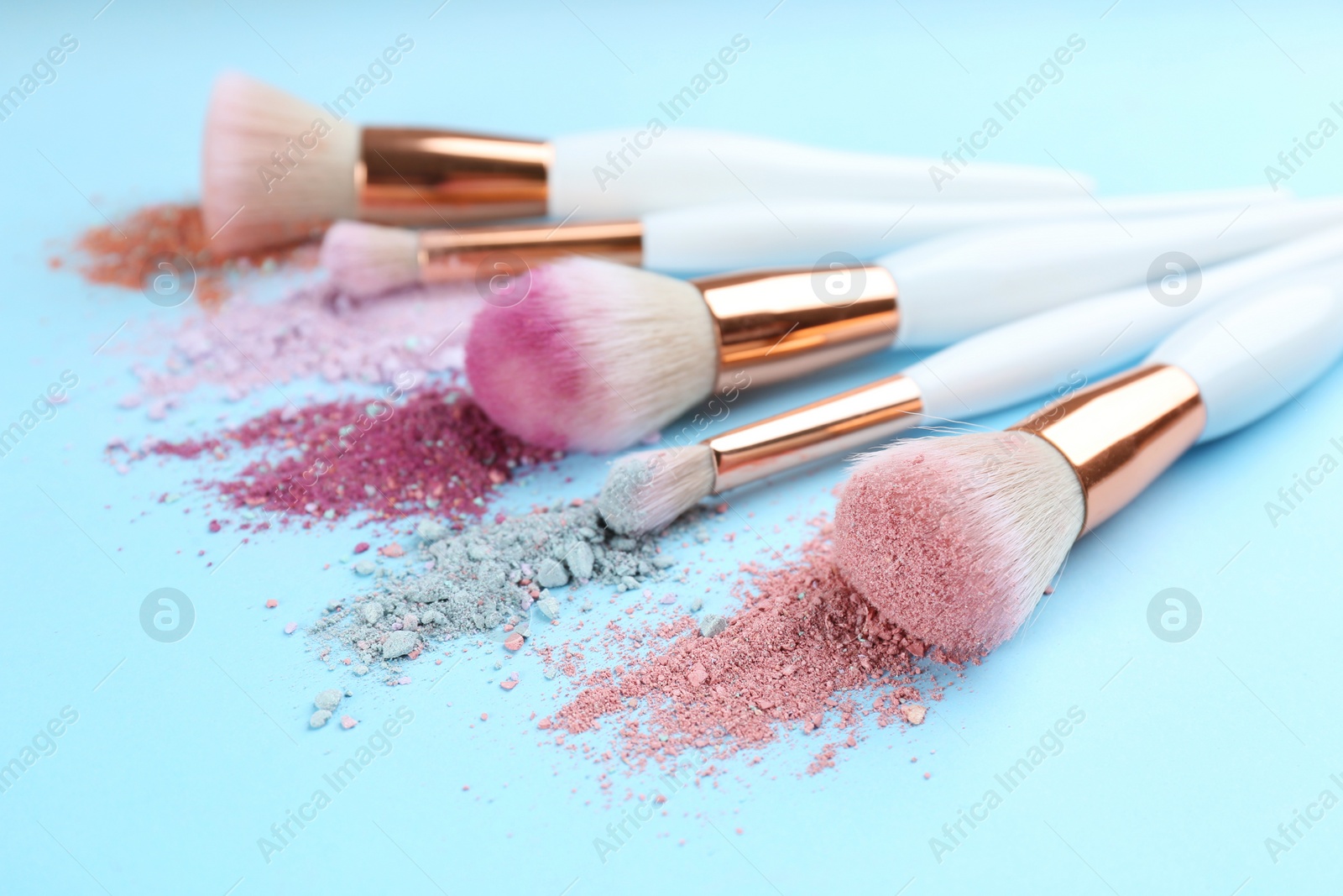 Photo of Different makeup brushes with crushed cosmetic products on light blue background, closeup