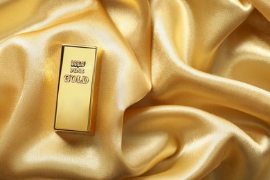 Photo of Gold bar on shiny silk fabric, top view. Space for text