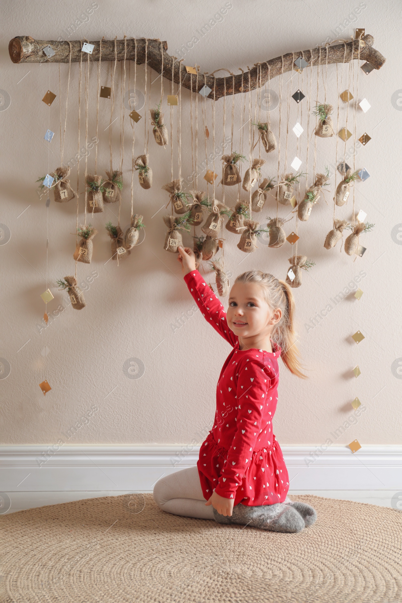 Photo of Little girl taking gift from New Year advent calendar indoors