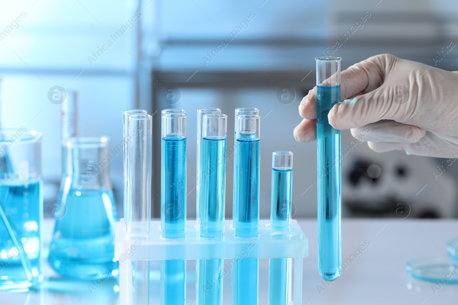 Photo of Scientist taking test tube with light blue liquid in laboratory, closeup