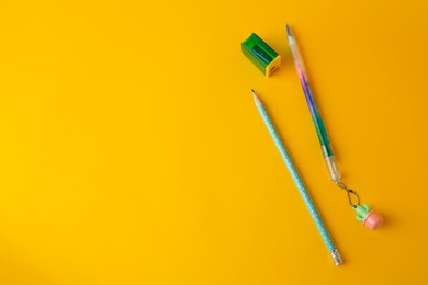 Erasable pen, pencil and sharpener on yellow background, flat lay. Space for text