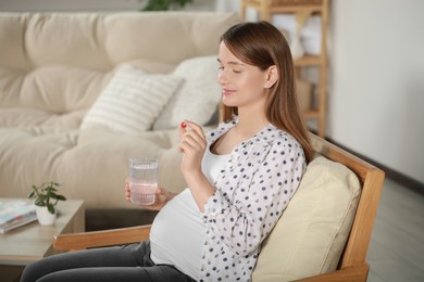 Photo of Beautiful pregnant woman holding pill and glass of water at home